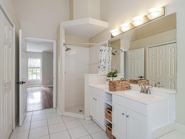 bathroom with double vanity, a tile shower, a sink, and tile patterned floors