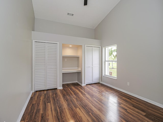 unfurnished bedroom featuring baseboards, visible vents, dark wood-style floors, high vaulted ceiling, and multiple closets