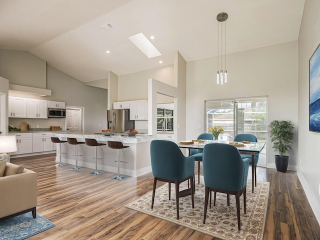 dining area featuring high vaulted ceiling, a skylight, wood finished floors, and baseboards