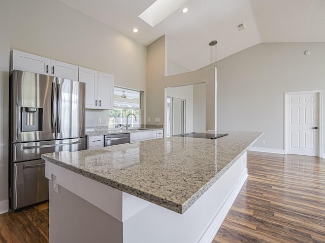 kitchen with a skylight, white cabinets, appliances with stainless steel finishes, light stone counters, and high vaulted ceiling