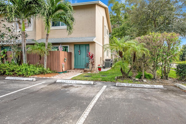 exterior space featuring uncovered parking, central air condition unit, fence, and stucco siding