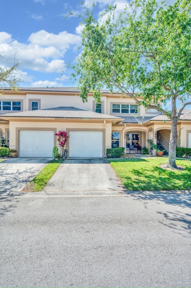 townhome / multi-family property with a garage, a front yard, driveway, and stucco siding