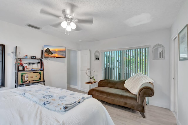 bedroom featuring a textured ceiling, ceiling fan, visible vents, baseboards, and wood tiled floor