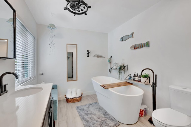 bathroom featuring toilet, wood finished floors, vanity, baseboards, and a soaking tub