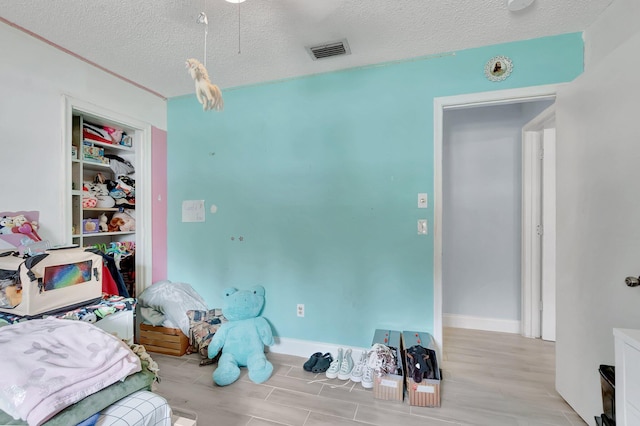 bedroom featuring a textured ceiling, wood finished floors, visible vents, and baseboards