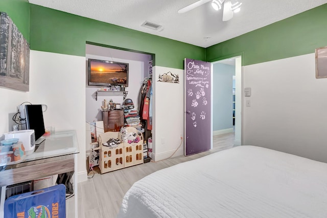 bedroom with a textured ceiling, wood finished floors, visible vents, and a ceiling fan