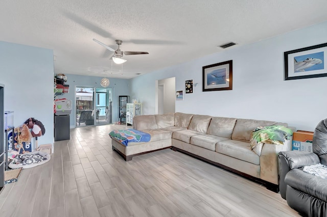 living room with a textured ceiling, a ceiling fan, visible vents, and light wood-style floors