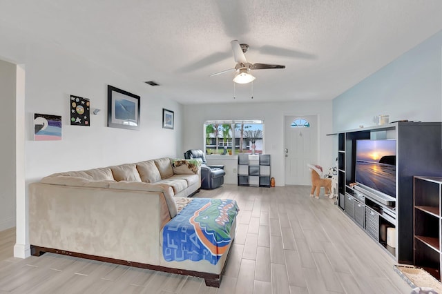 living area with a textured ceiling, visible vents, wood finished floors, and a ceiling fan