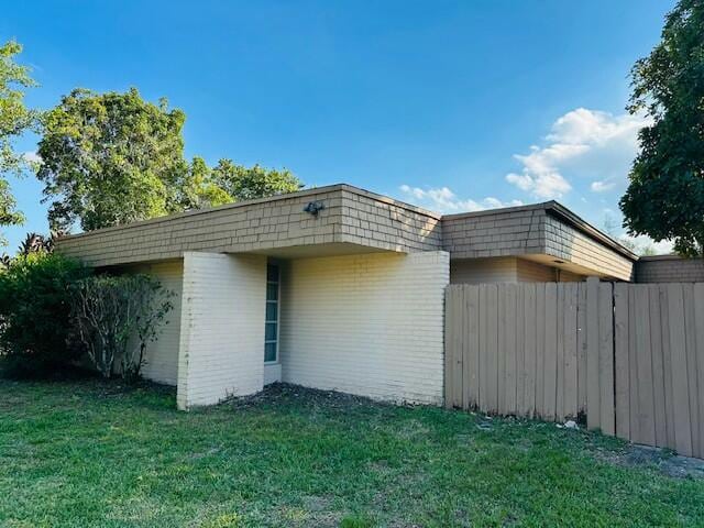 view of home's exterior featuring brick siding, a yard, and fence