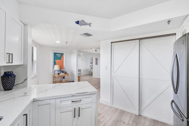 kitchen featuring freestanding refrigerator, light stone counters, visible vents, and light wood-style floors