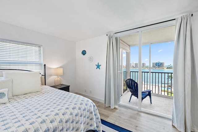 bedroom with baseboards, light wood finished floors, a view of city, a water view, and access to outside