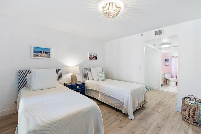 bedroom featuring ensuite bathroom, baseboards, visible vents, and wood finished floors