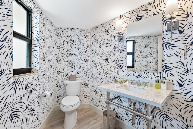 bathroom with wallpapered walls, toilet, baseboards, a sink, and wood finished floors