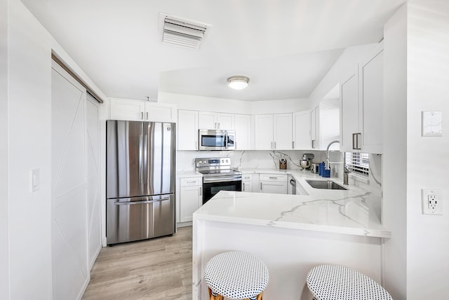 kitchen featuring a sink, a peninsula, light stone counters, visible vents, and appliances with stainless steel finishes