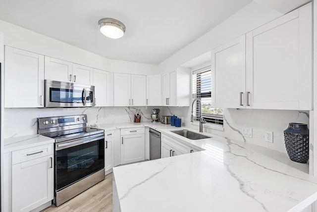 kitchen with light wood finished floors, a sink, white cabinetry, light stone countertops, and appliances with stainless steel finishes