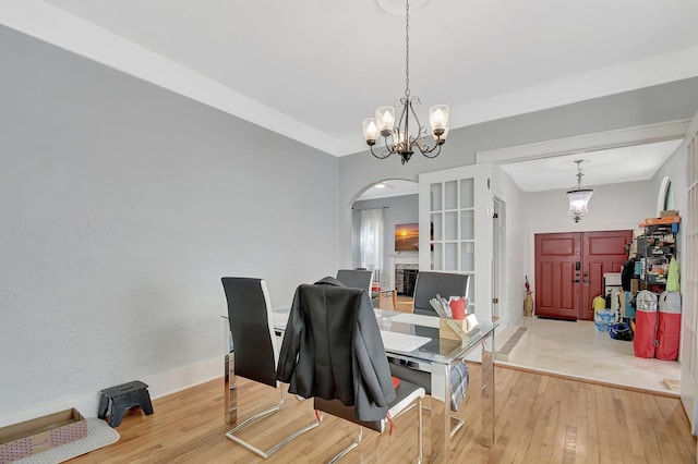 dining area with a chandelier, arched walkways, baseboards, and light wood finished floors