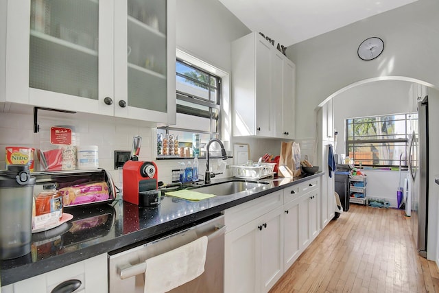 kitchen with a sink, white cabinets, light wood finished floors, appliances with stainless steel finishes, and tasteful backsplash