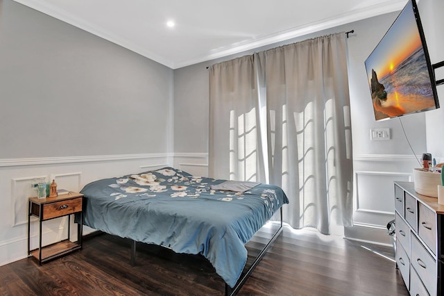 bedroom with a wainscoted wall, ornamental molding, dark wood finished floors, and a decorative wall