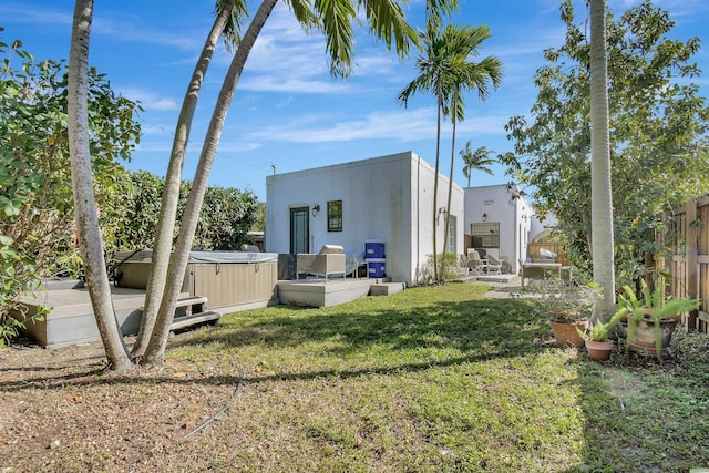 rear view of property with stucco siding, a hot tub, fence, and a yard