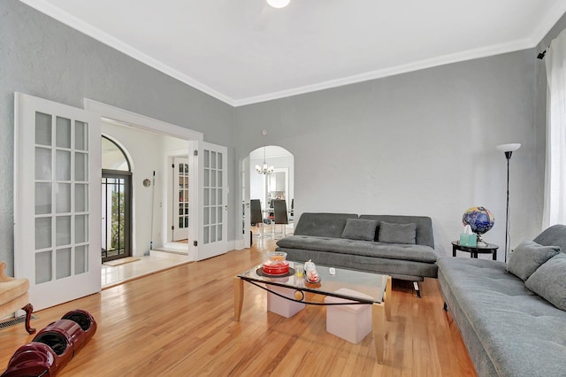 living area featuring arched walkways, french doors, an inviting chandelier, ornamental molding, and light wood-type flooring