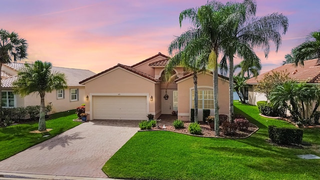 mediterranean / spanish-style home featuring decorative driveway, a yard, stucco siding, a garage, and a tiled roof