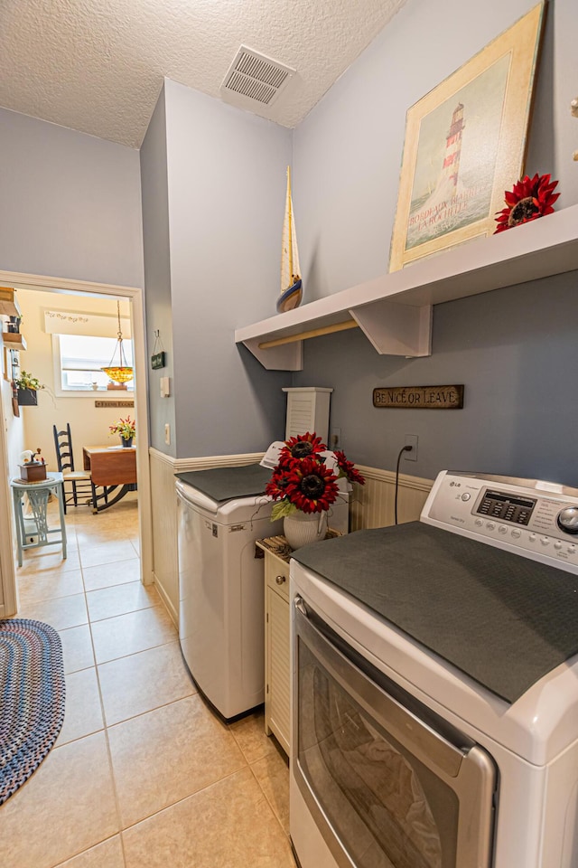 laundry room featuring light tile patterned floors, a textured ceiling, laundry area, visible vents, and washing machine and clothes dryer