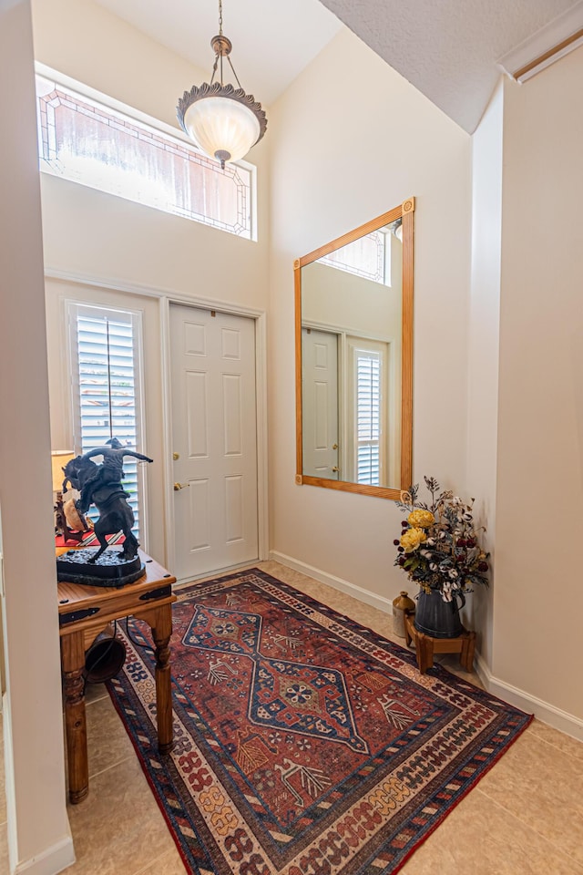 entryway with tile patterned floors, a towering ceiling, and baseboards