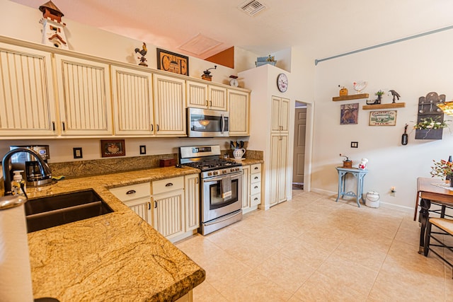 kitchen with visible vents, appliances with stainless steel finishes, light stone counters, cream cabinetry, and a sink