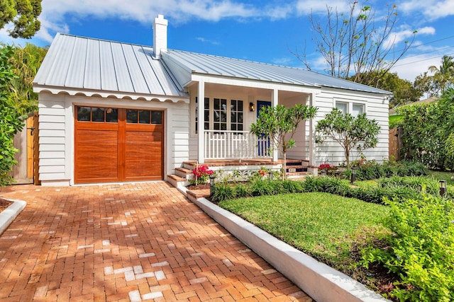 view of front of property with metal roof, a porch, an attached garage, a standing seam roof, and a chimney