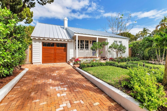 view of front of property with metal roof, a porch, an attached garage, decorative driveway, and a chimney