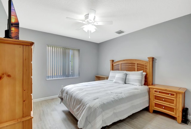 bedroom featuring a ceiling fan, visible vents, baseboards, and wood finished floors