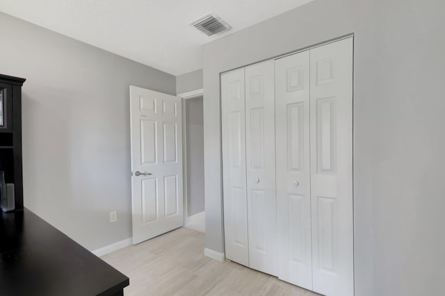 bedroom with light wood-type flooring, baseboards, visible vents, and a closet