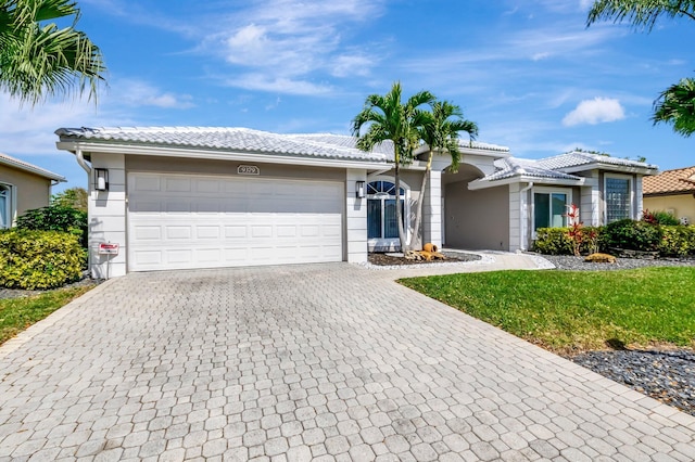 ranch-style home featuring decorative driveway, an attached garage, a tile roof, and stucco siding