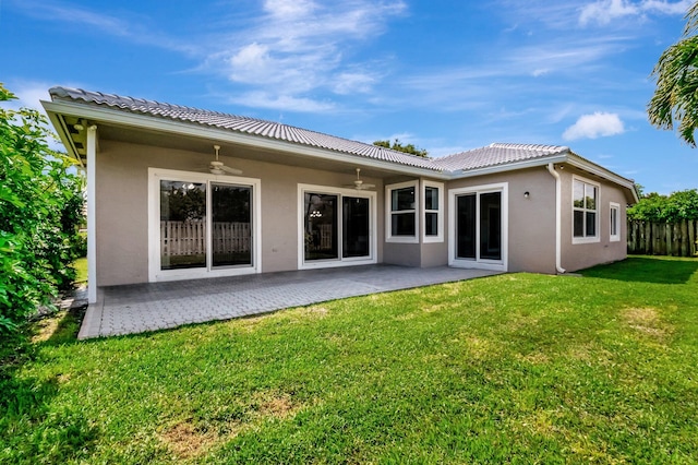 rear view of house with ceiling fan, fence, a lawn, stucco siding, and a patio area