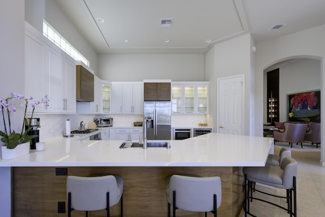 kitchen with a peninsula, glass insert cabinets, stainless steel fridge, and visible vents