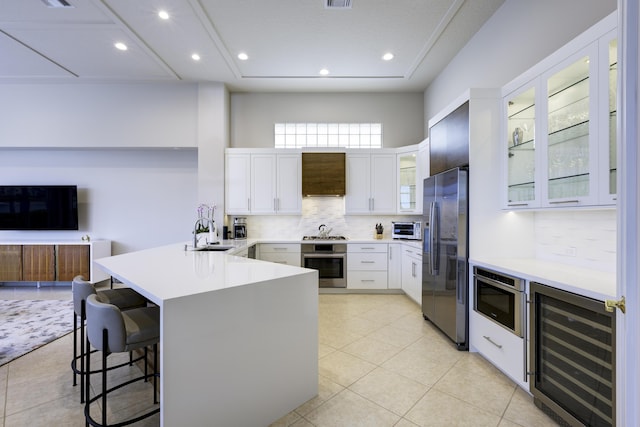 kitchen with wine cooler, appliances with stainless steel finishes, a sink, wall chimney range hood, and a peninsula