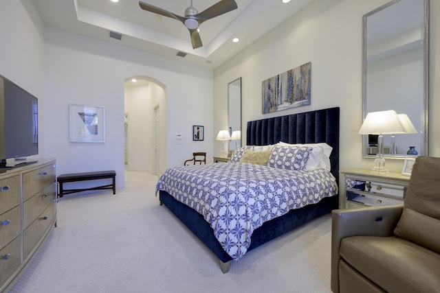 bedroom with visible vents, arched walkways, a raised ceiling, light colored carpet, and recessed lighting