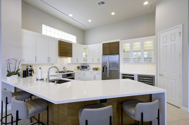 kitchen with stainless steel fridge, visible vents, a peninsula, a kitchen bar, and a sink