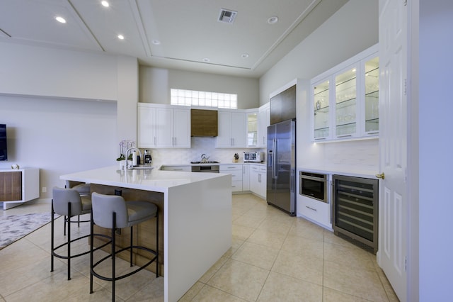 kitchen with a breakfast bar, stainless steel refrigerator with ice dispenser, glass insert cabinets, beverage cooler, and a peninsula