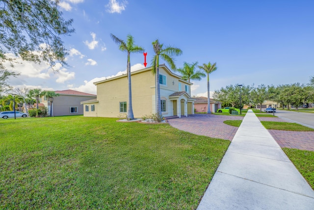 view of side of home featuring an attached garage, decorative driveway, a lawn, and stucco siding