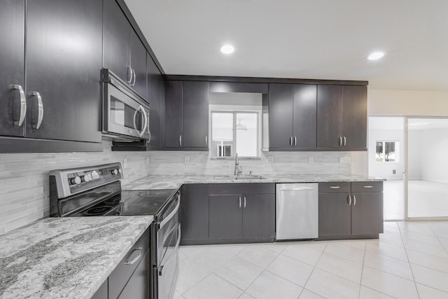 kitchen with tasteful backsplash, light stone counters, stainless steel appliances, and a sink