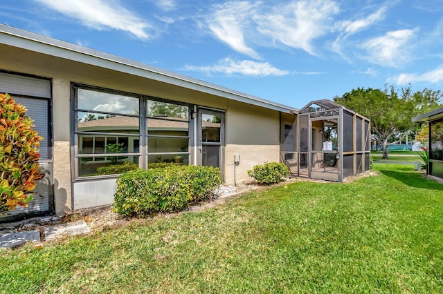 rear view of house with a lanai, a lawn, and stucco siding