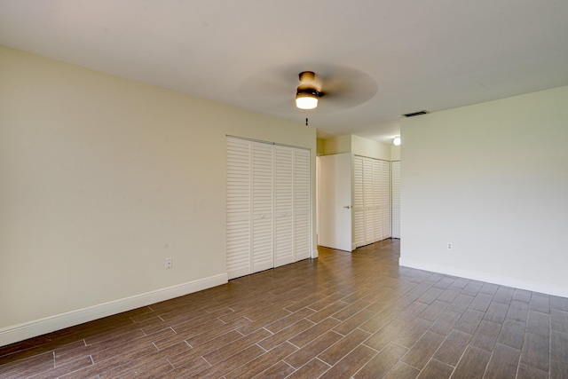 unfurnished room with dark wood-style floors, visible vents, baseboards, and a ceiling fan