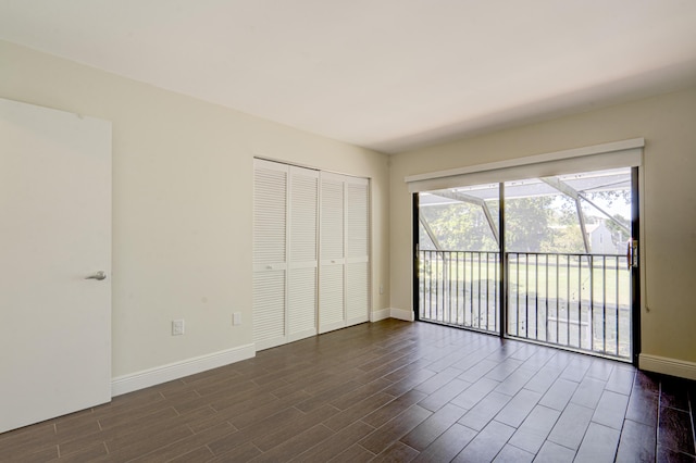 unfurnished bedroom with baseboards, a closet, dark wood finished floors, and access to exterior