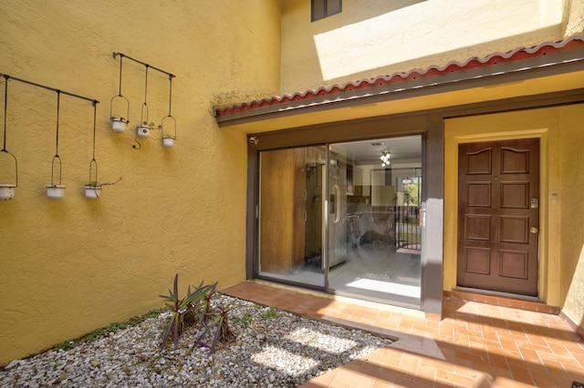 property entrance with a tile roof, visible vents, and stucco siding