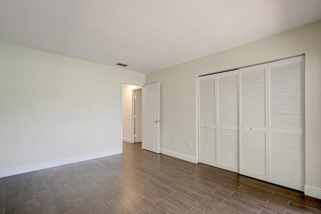 unfurnished bedroom featuring a closet, dark wood-style flooring, visible vents, and baseboards