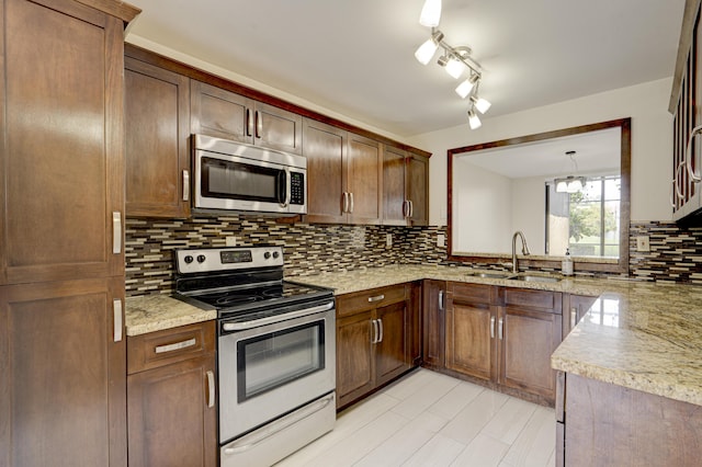 kitchen with light stone counters, decorative light fixtures, a sink, stainless steel appliances, and backsplash