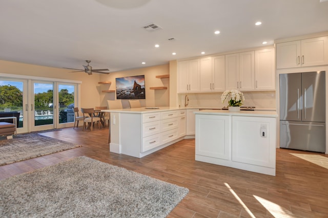 kitchen featuring stainless steel fridge, visible vents, wood finished floors, light countertops, and a sink