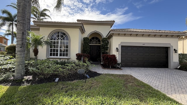 mediterranean / spanish-style house featuring an attached garage, a tile roof, decorative driveway, and stucco siding