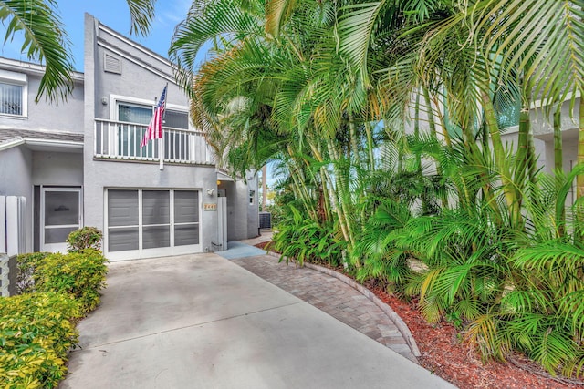 view of side of property featuring driveway, a balcony, an attached garage, and stucco siding